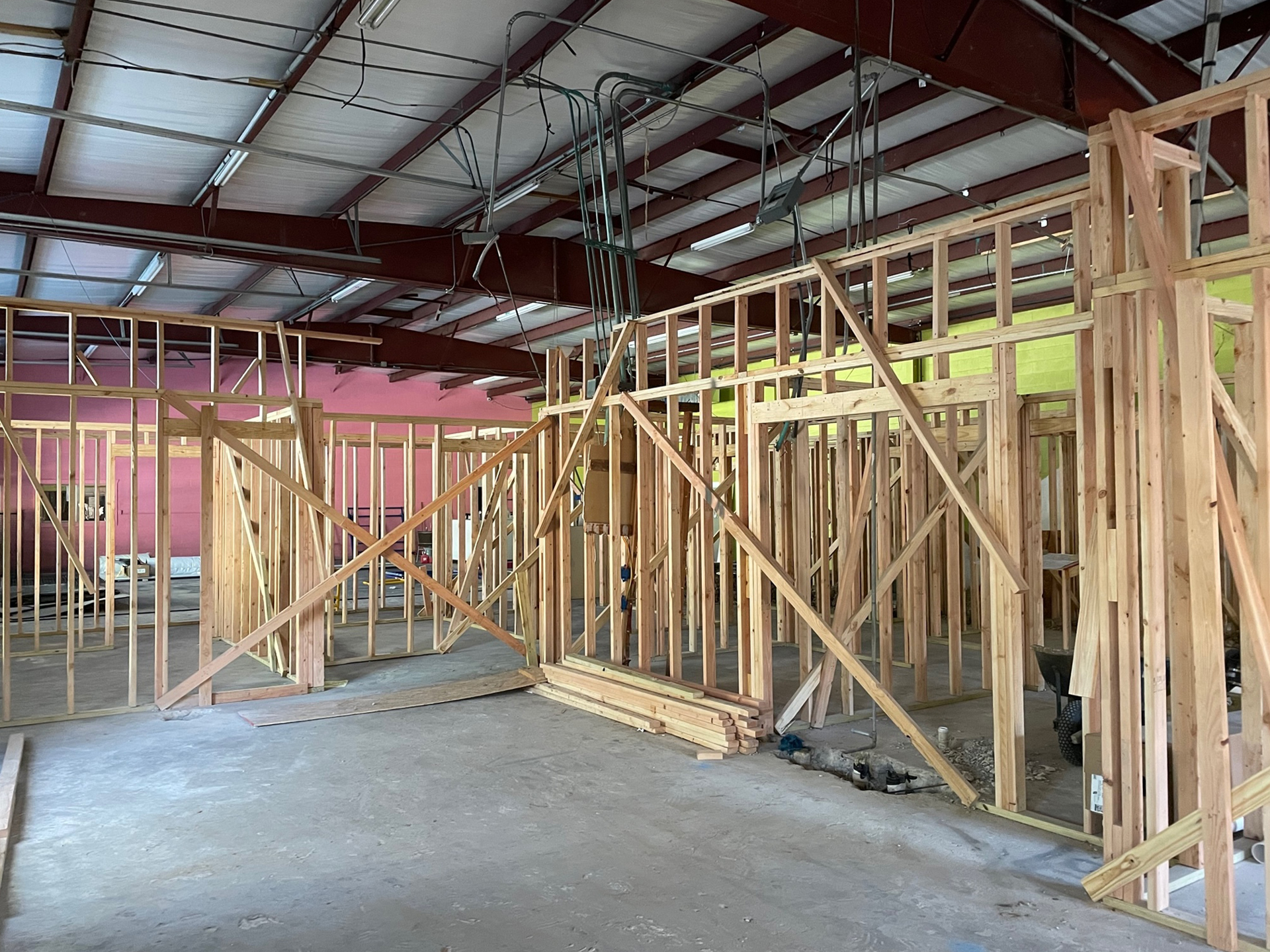 Interior of a building under construction with wooden stud framing erected, showing exposed beams and wiring against a background of a red ceiling and walls, designed for veterinary care in Houston.