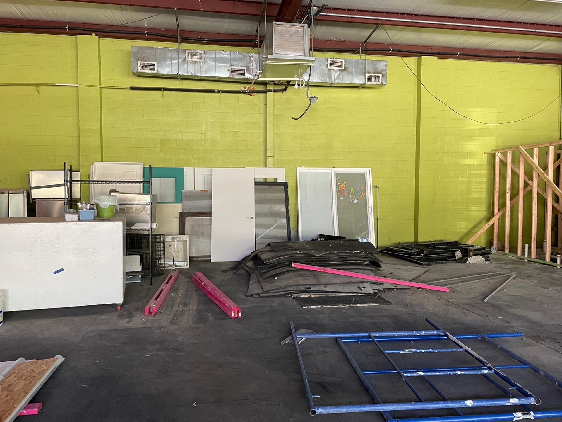 Interior of an industrial building with green walls, featuring scattered construction materials, including metal frames, wooden planks, and insulation panels designed for veterinary care facilities.