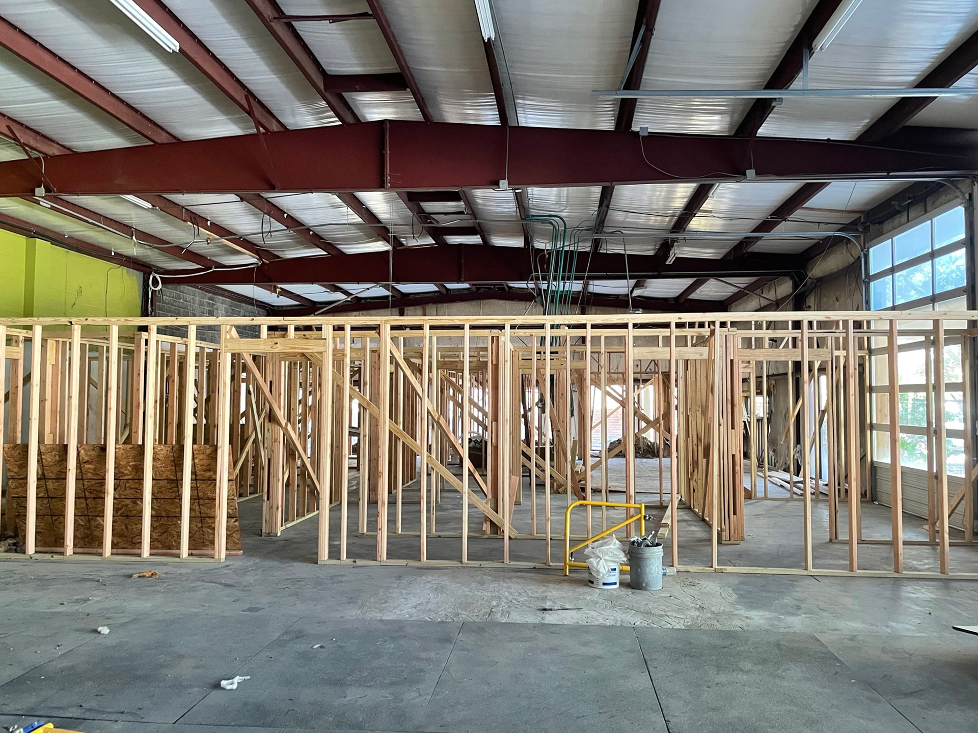 Interior of a warehouse under construction with wooden stud framing in progress, insulation materials visible, and tools on the floor, under a metal roof with exposed beams for future pet rehabilitation services.