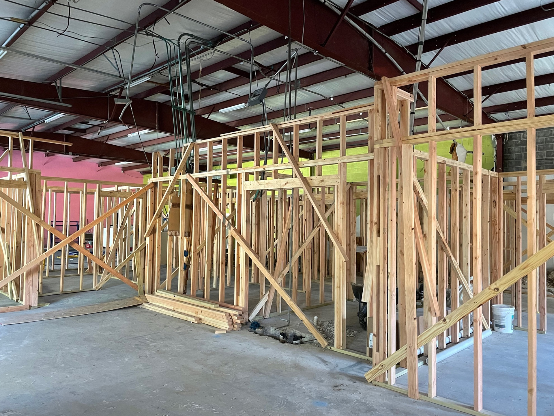 Interior view of a construction site showing wooden framing for walls under a metal roof, with exposed wires and pet rehabilitation materials scattered around.