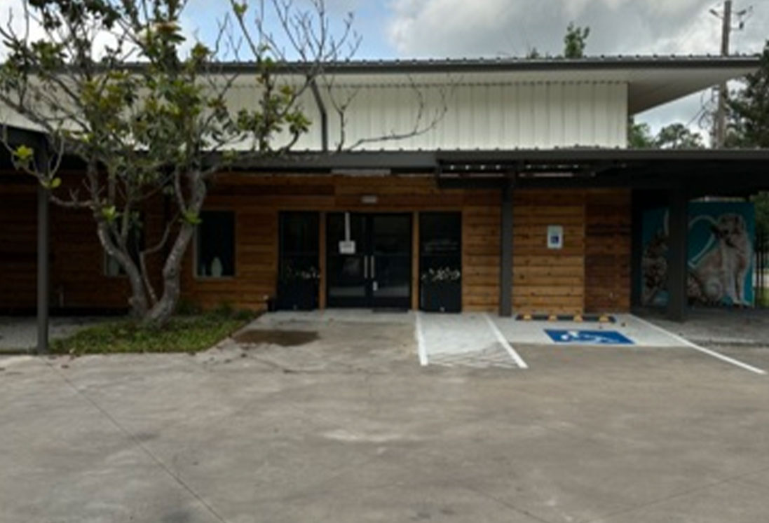 A small, rustic building with a wood-paneled exterior and a flat roof, featuring a central entrance flanked by windows dedicated to veterinary care in Houston. Two parking spaces including a handicapped spot are